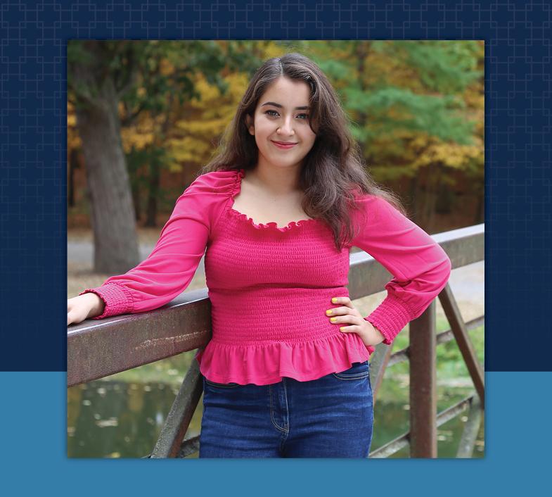 female with brown hair in bright pink shirt and blue jeans standing near fence